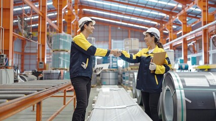 Two manufacturing employees standing and shaking hands while working at factory manufacturing success teamwork collaboration