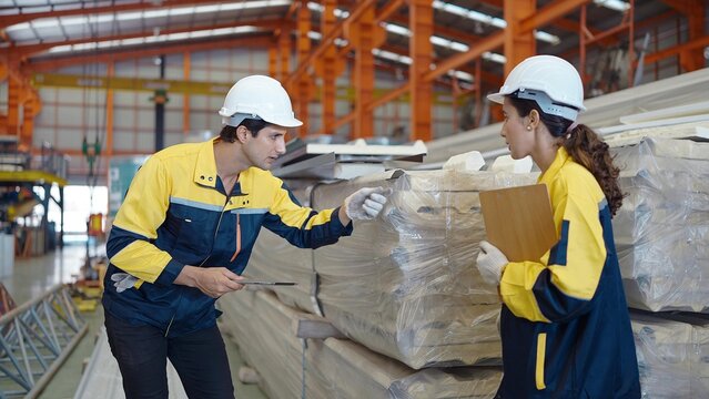 Two industrial worker in uniform holding tablet checking quality of metal sheet roof for industry construction at manufacturing factory