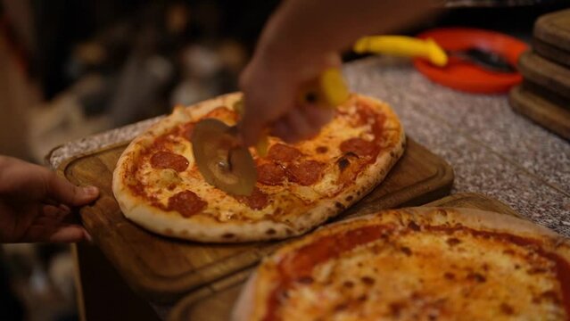 Close up of anonimous pizza chef slicing appetising pepperoni pizza with cutter wheel in order to be served in the restaurant