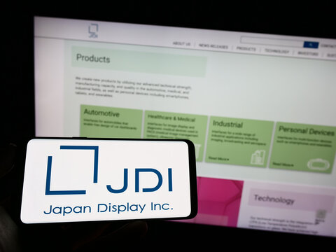 Stuttgart, Germany - 04-23-2023: Person holding mobile phone with logo of electronics company Japan Display Inc. (JDI) on screen in front of web page. Focus on phone display.