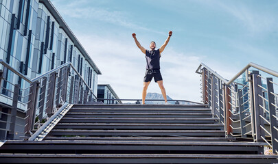 First place belongs to me. Low angle shot of a sporty young man cheering at the top of a staircase while exercising outdoors.