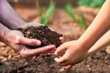 Generations sharing the earth. Father offering soil to his son hands on a plantation