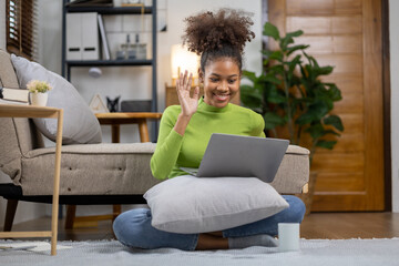 A young American woman is video calling with her friends in her living room, she spends her weekend relaxing at home playing social media and watching movies. The idea of living on vacation.