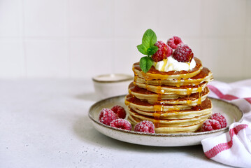 Delicious homemade pancakes with whipped cream, maple syrup and raspberry for a breakfast.