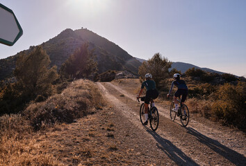 Back view of professional gravel cyclists riding uphill with mountain view at sunset. Alicante...