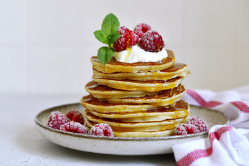 Delicious homemade pancakes with whipped cream, maple syrup and raspberry for a breakfast.