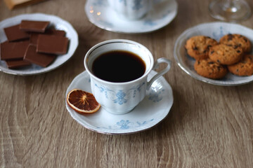 Cup of tea or coffee, plate of cookies, cup of blueberries, plate of chocolate, glass of juice, book, reading glasses, teapot, flowers and lit candles on the table. Brunch or afternoon tea concept.