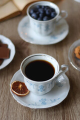 Cup of tea or coffee, plate of cookies, cup of blueberries, plate of chocolate, glass of juice, book, reading glasses, teapot, flowers and lit candles on the table. Brunch or afternoon tea concept.