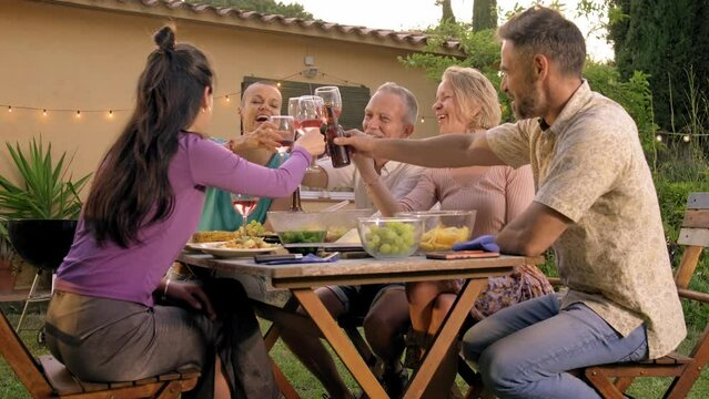Group of people enjoying meal outdoors. Happy friends toasting with wine during barbecue garden dinner party. 4k video. 