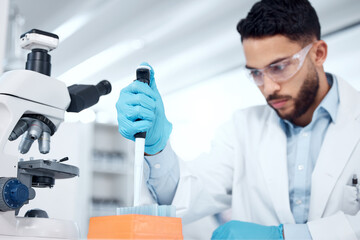 One mixed race male scientists wearing safety goggles and a labcoat while conducting medical research experiments with pipette and test tubes in a lab. Recording his findings for future investigation