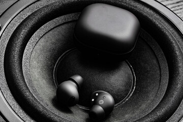 black wireless earpone buds on speakers background