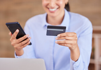 Unrecognizable mixed race businesswoman smiling while using a phone and credit card sitting alone in an office at work. Happy hispanic female shopping online and paying with her card