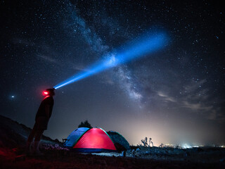 Persona con una linterna bajo las estrellas acampa en la montaña con tienda de campaña. - obrazy, fototapety, plakaty