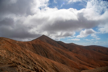 Fototapeta na wymiar Detalle de una impresionante montaña rocosa de origen volcánico con una cumbre muy puntiaguda en medio de un paisaje desértico en la turística isla de Fuerteventura en las Islas Canarias.