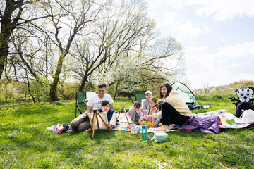 Happy young family with four children having fun and enjoying outdoor on picnic blanket painting at garden spring park, relaxation.