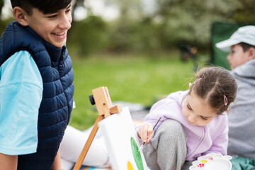 Happy young family, сhildren having fun and enjoying outdoor on picnic blanket painting at garden spring park, relaxation.