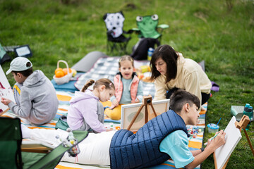Happy young family, mother and children having fun and enjoying outdoor on picnic blanket painting at garden spring park, relaxation.