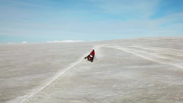 Aerial view of a person doing stunts on a snowmobile, on the surface of a glacier in Iceland, on a sunny day