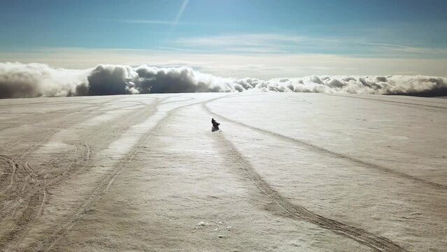 Aerial panoramic view of a person riding a snowmobile on a glacier in Iceland, over the clouds, on a sunny day