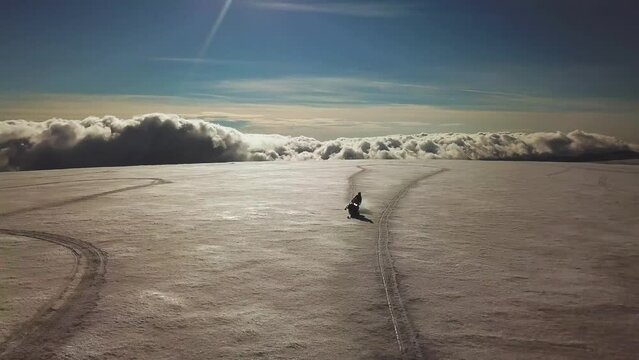 Aerial view of a person doing stunts on a snowmobile, on a glacier in Iceland, over the clouds, on a sunny day