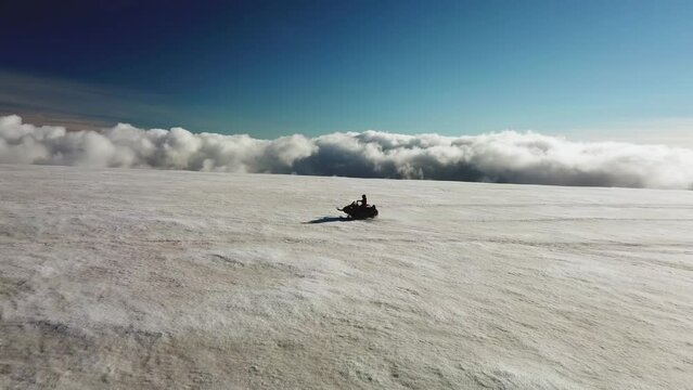 Aerial landscape view of a person riding a snowmobile on a glacier in Iceland, over the clouds, on a sunny day
