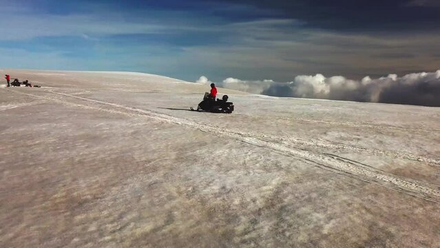 Aerial landscape view of a person riding a snowmobile on the surface of a glacier in Iceland, over the clouds, on a sunny day