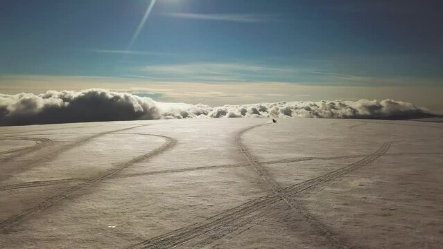 Aerial view of a person riding a snowmobile on the surface of a glacier in Iceland, over the clouds, on a sunny day