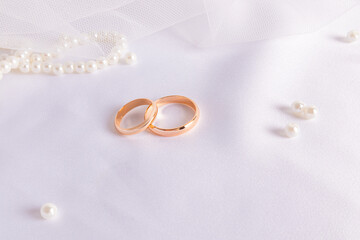 Two gold wedding rings on white satin textiles with pearl beads. Wedding festive background. A copy...