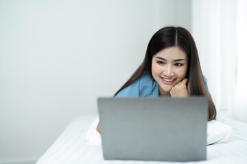 Beautiful young woman relaxing on a bed use a laptop to play social media at home