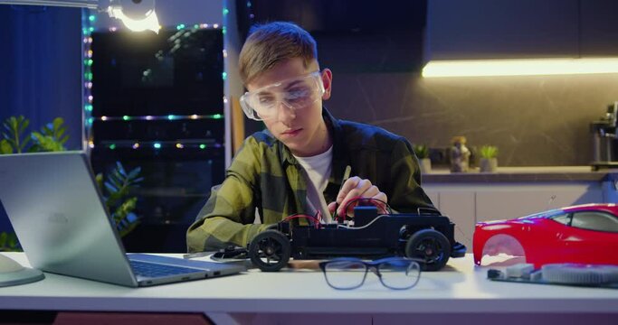 Smart kid assembling and testing electric circuit building and programming car. Boy repairing his remote controlled toy car with a tool in hand and carefully assembles toy car with screwdriver.