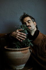 a young brown-haired man smelling his marijuana plant at home