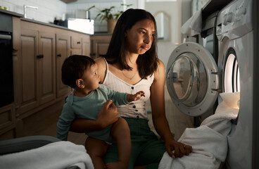 Adulting is like a 247 job. Shot of a mom doing laundry at night with her baby on her arm.