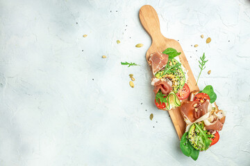Open sandwich with prosciutto or jamon, avocado and fresh greens on a wooden board. Keto breakfast...