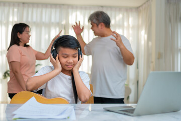 Fototapeta premium Asian boy kid wearing headphones and play loud music. so as not to hear quarrel while parents having fight or quarrel conflict at home. Unhappy problem in family, Domestic problems in the family.
