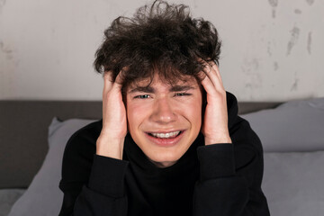 A severely depressed teenager, sitting on the bed, holding his head. A young man in a hard mental condition.