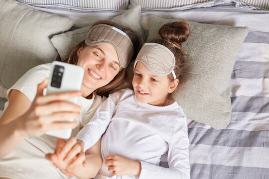 Top view of smiling happy family waking up in morning lying in bed in sleeping masks and making selfie woman holding smart phone in hands taking picture.