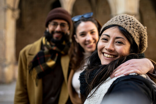 group of happy friends making a selfie in the street, focus on girl. three cheerful travelers taking a photo on their holidays. toursit concept.