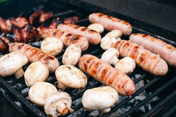 Frying sausages and mushrooms on the grill. Summer outdoor party with open fire.
