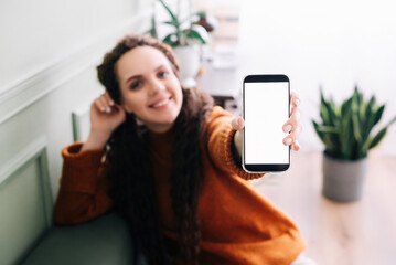 Happy young woman holding mobile phone to showcase blank display for app advertising. Smartphone mockup screen for advertising digital application with woman's hand.