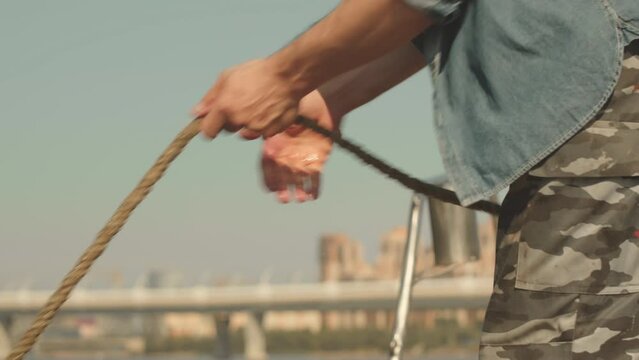 Cropped shot of unrecognizable sailor in khaki pants taking mooring ball on rope out of water on hot sunny day