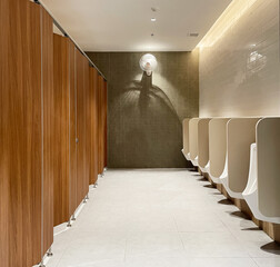 Minimal style and modern beautiful interior design of public restroom with row of urinals, wooden toilet doors, bright light, ceramic wall and fllor and ventilation fan.