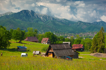 Bacówka na Olczy w Zakopanem. Górskie domy wśród zielonej trawy na tle gór i zachmurzonego...