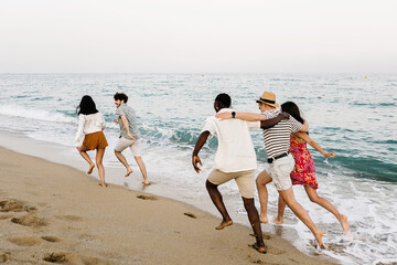 Young group of people running on the beach. Diverse happy friends enjoying summer vacation together. Summertime concept