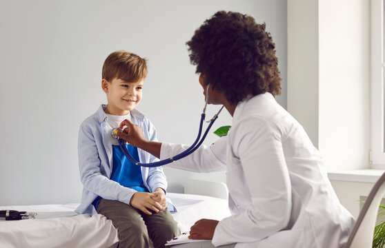African American pediatrician listening to heartbeat of boy patient with stethoscope. Female doctor, general practitioner examining cute boy in medical clinic. Treatment and healthcare concept