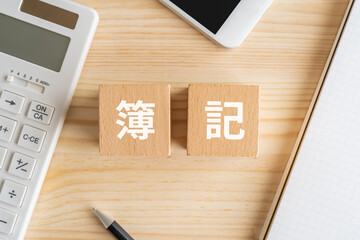 簿記と書かれたブロック、電卓、スマホ、ノート、ペン