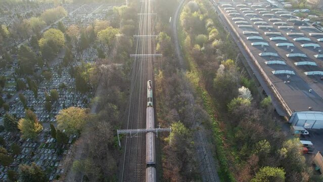 A morning drone-shot of a freight train passing through the city, on a viaduct over green terrain. The locomotive pulls empty wagons to be loaded with raw materials.