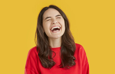 Studio shot of happy laughing woman. Pretty young girl in red sweatshirt standing isolated on bright yellow background and laughing happily at very funny joke. Laughter, emotion concept