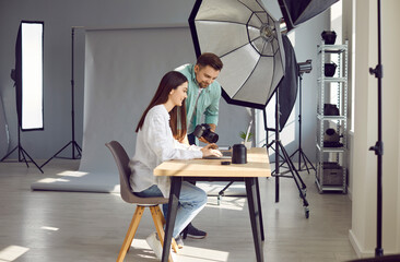 Male photographer showing photo on laptop to model choosing photos together. Professional photographers and attractive young woman choosing best photos during photoshoot in studio