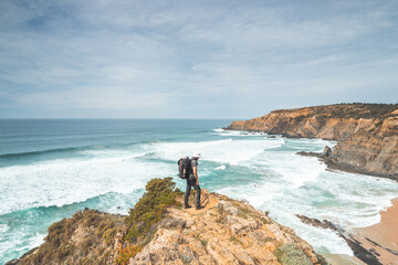 Hiker and adventurer stand on a rugged rock and cliff coastline and enjoy the view on the Atlantic...