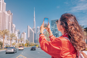 Tourist happy girl taking photos for her travel blog, in Dubai downtown district against background...